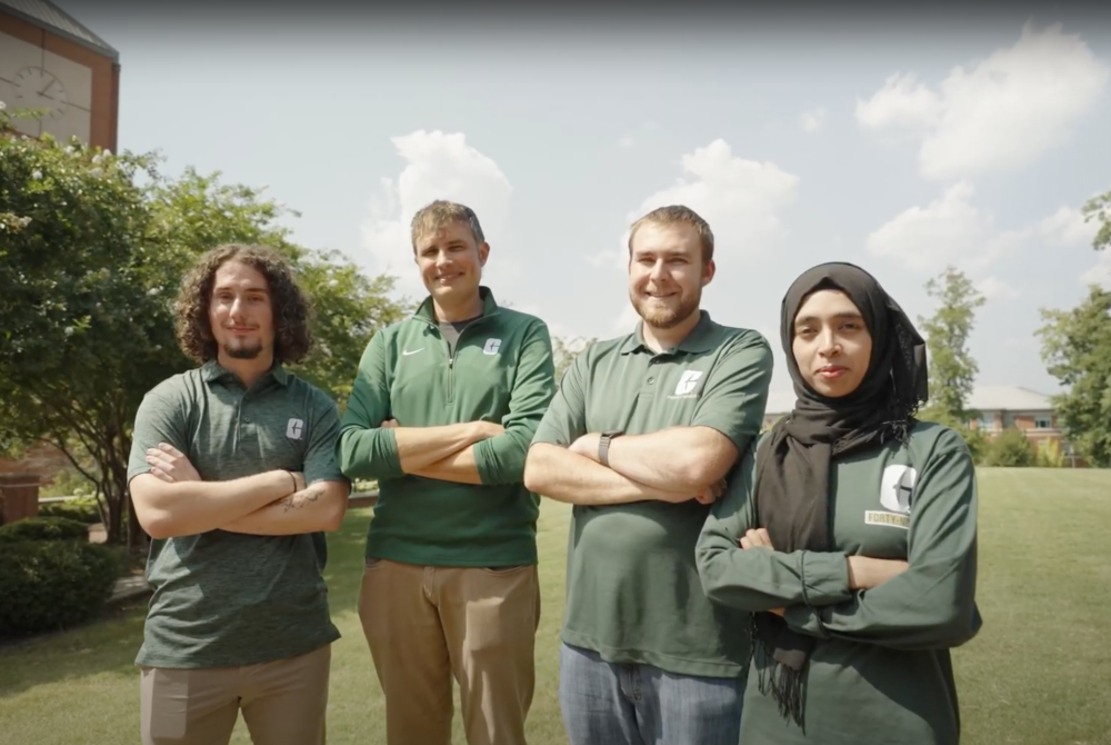 4 people smiling with arms cross in Charlotte 49ers gear.